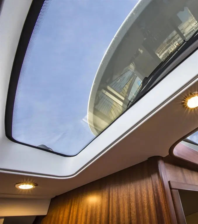 A modern boat interior featuring a panoramic skylight, showcasing blue sky and cloud reflections, with warm lighting.